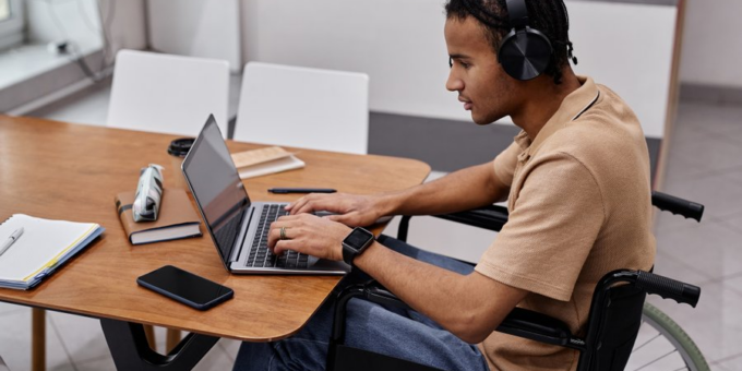 Student wearing headphones while working on a laptop computer, seated in a wheelchair