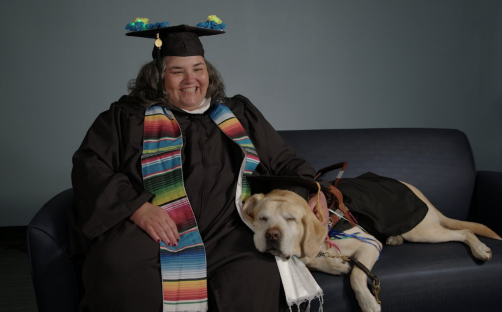 SNHU graduate smiling, seated on couch with service dog