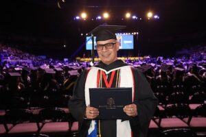 SNHU graduate Jeff Mendez smiling at the camera, holding his diploma at commencement