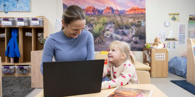 Teacher and student sitting at a desk on a laptop smiling