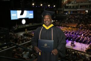 Bobby at commencement holding his diploma and smiling at the camera
