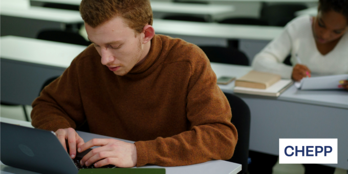 Student sitting at a desk typing on their laptop in a classroom.