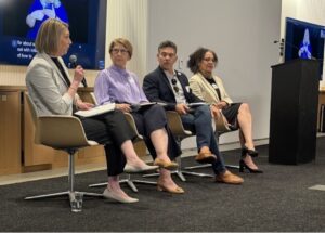 3 panelists sitting on the stage and a person with a microphone interviewing them.