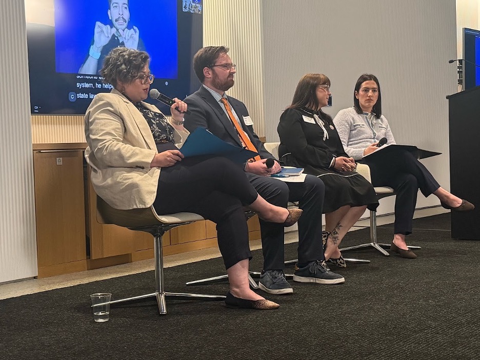 3 panelists sitting on the stage and a person with a microphone interviewing them.